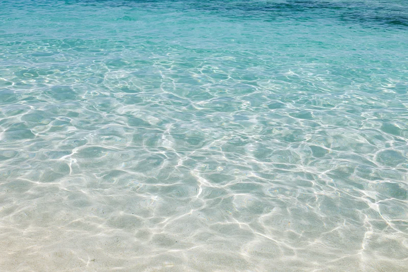 Clear turquoise ocean water rippling over white sand at shallow beach