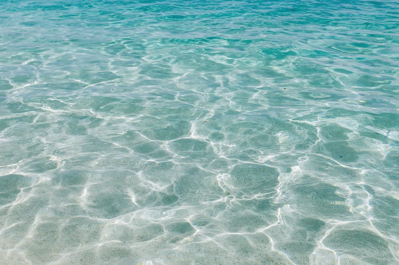 Clear shallow turquoise ocean water rippling over sandy seabed in sunlight