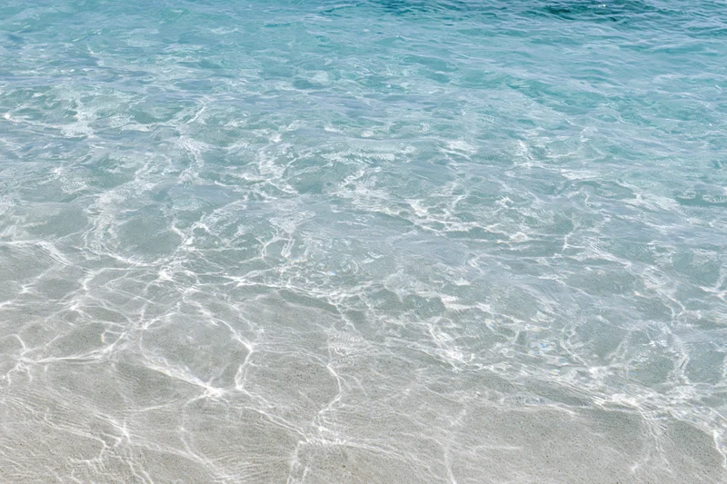 Clear ocean water rippling over sandy beach under sunlight