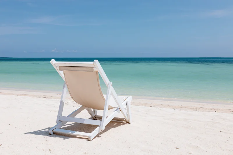 White lounge chair on sandy beach facing turquoise ocean under clear blue sky