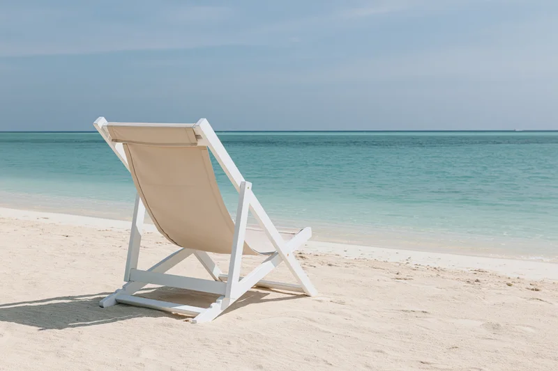 White lounge chair reclining on sandy beach facing turquoise ocean