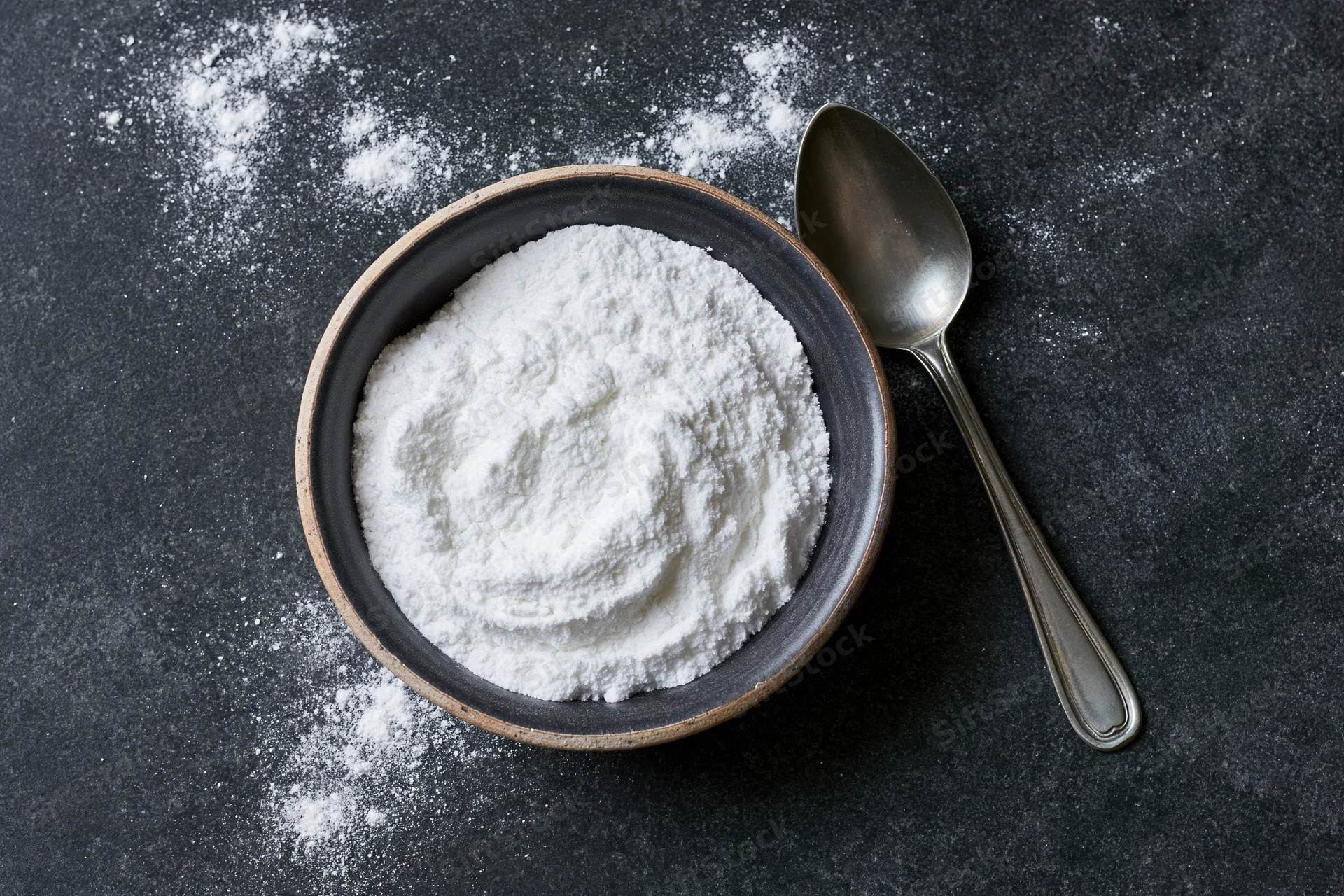 Flour in a ceramic bowl with a metal spoon on a dark surface