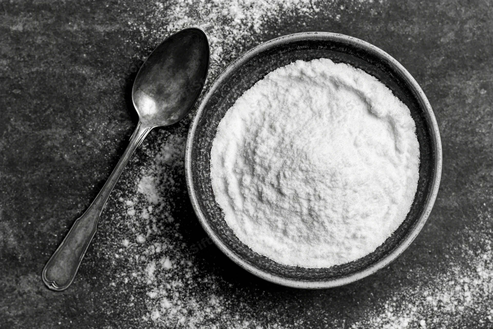 Bowl of flour with spoon on dark surface