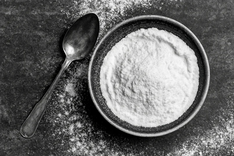 Bowl of flour with spoon on dark surface