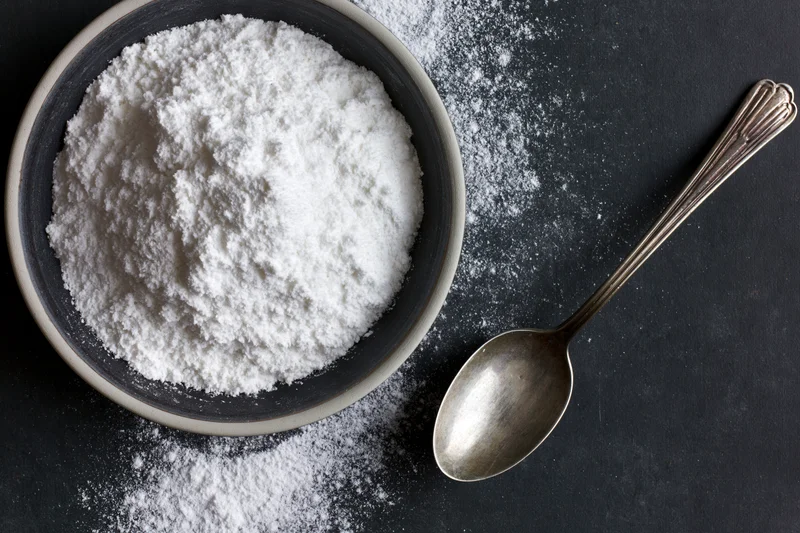 White powder in a ceramic bowl with a metal spoon on a dark surface