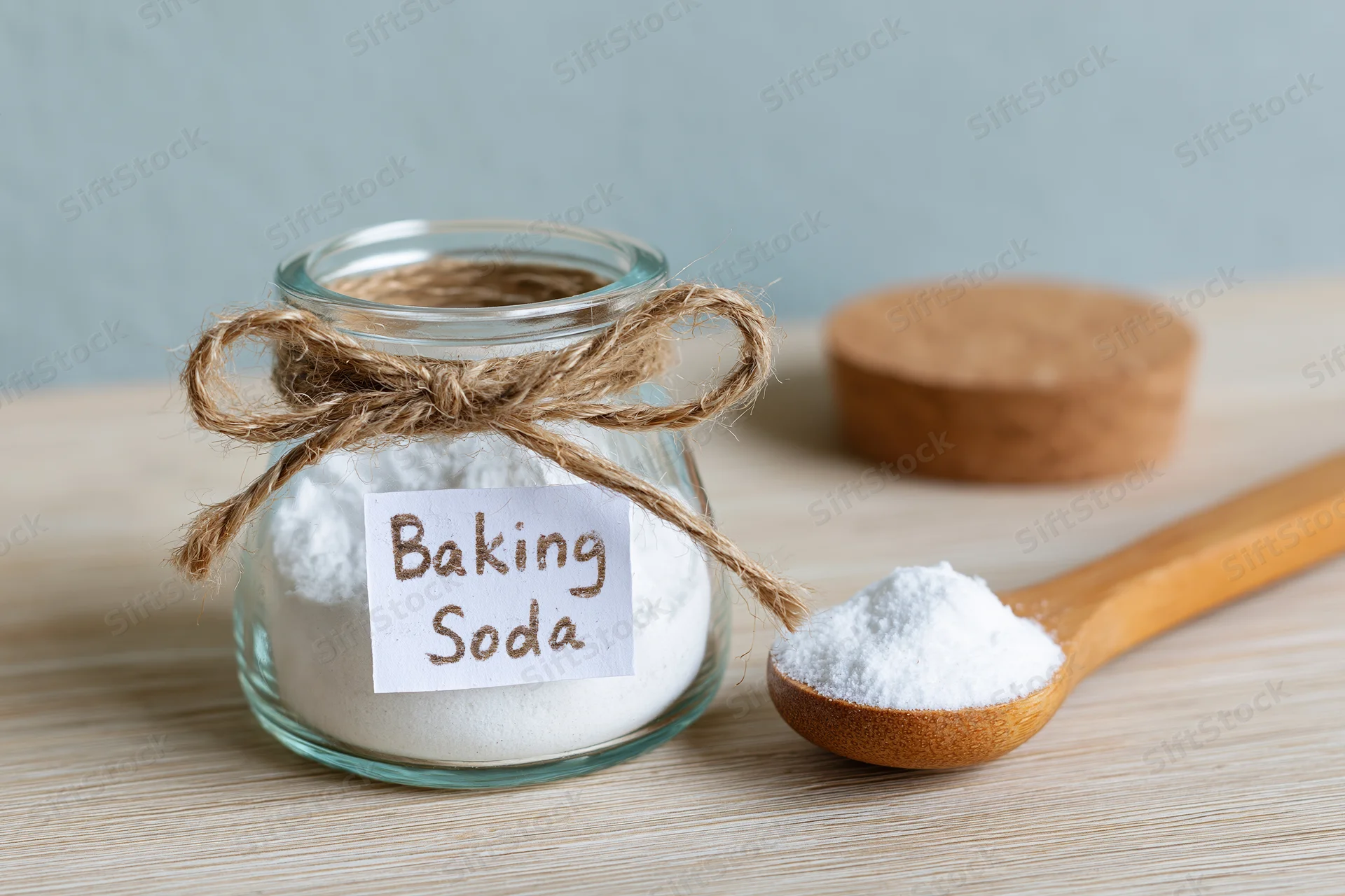 Glass jar labeled baking soda with wooden spoon holding powder on wooden countertop