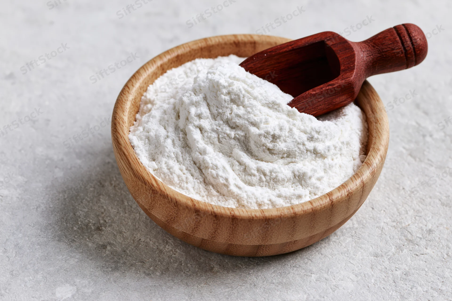 White flour in a wooden bowl with a scoop on a light surface