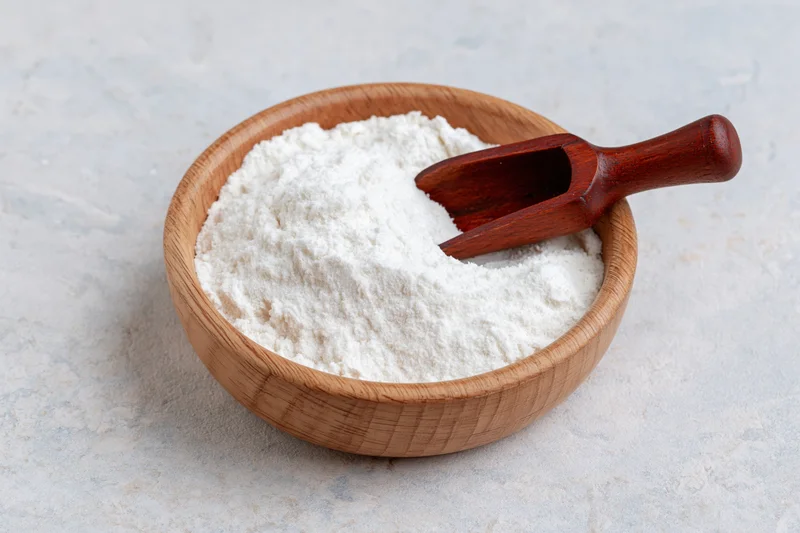 White flour in a wooden bowl with a scoop on a light countertop