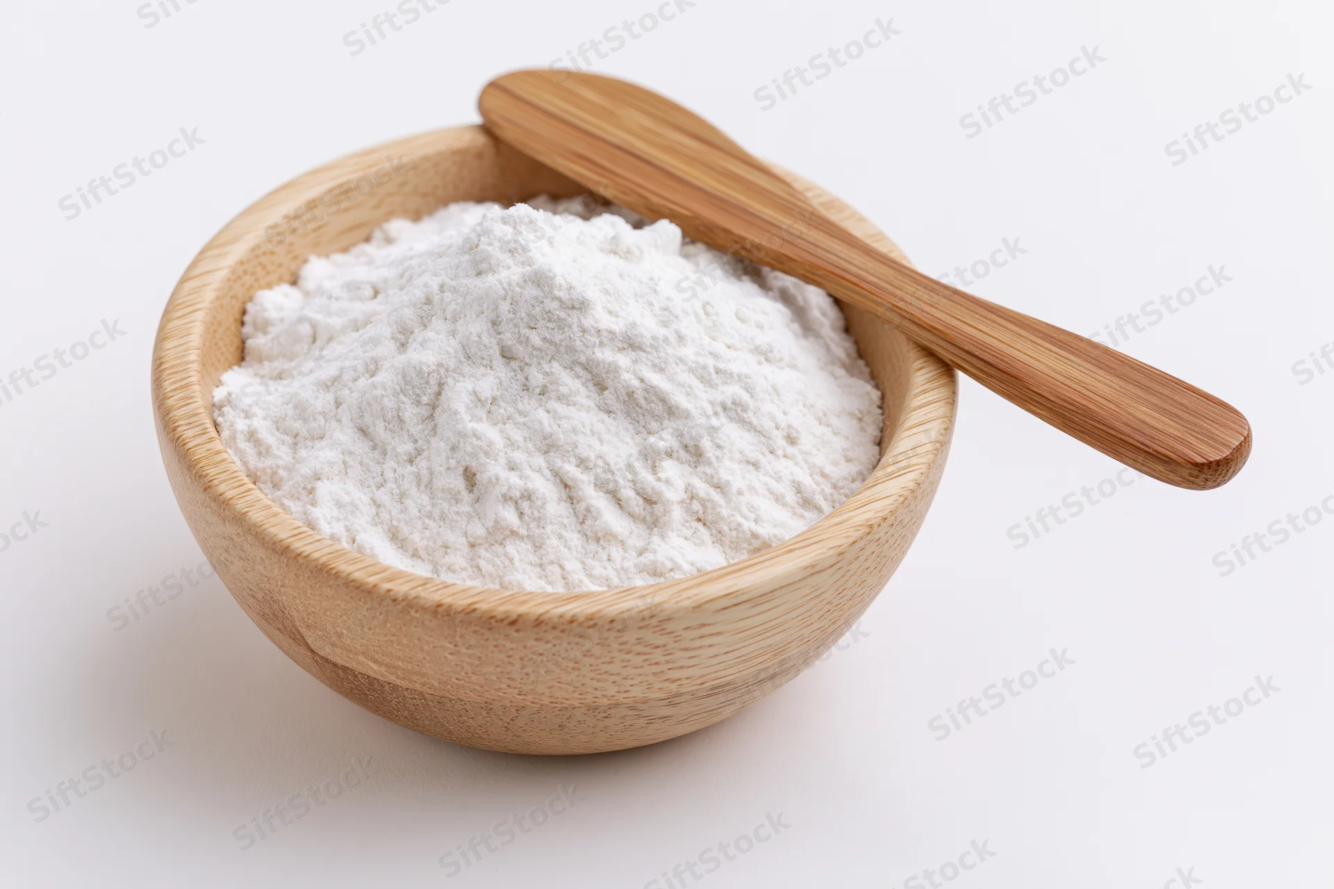 White flour in a bamboo bowl with a wooden spoon on a plain white surface
