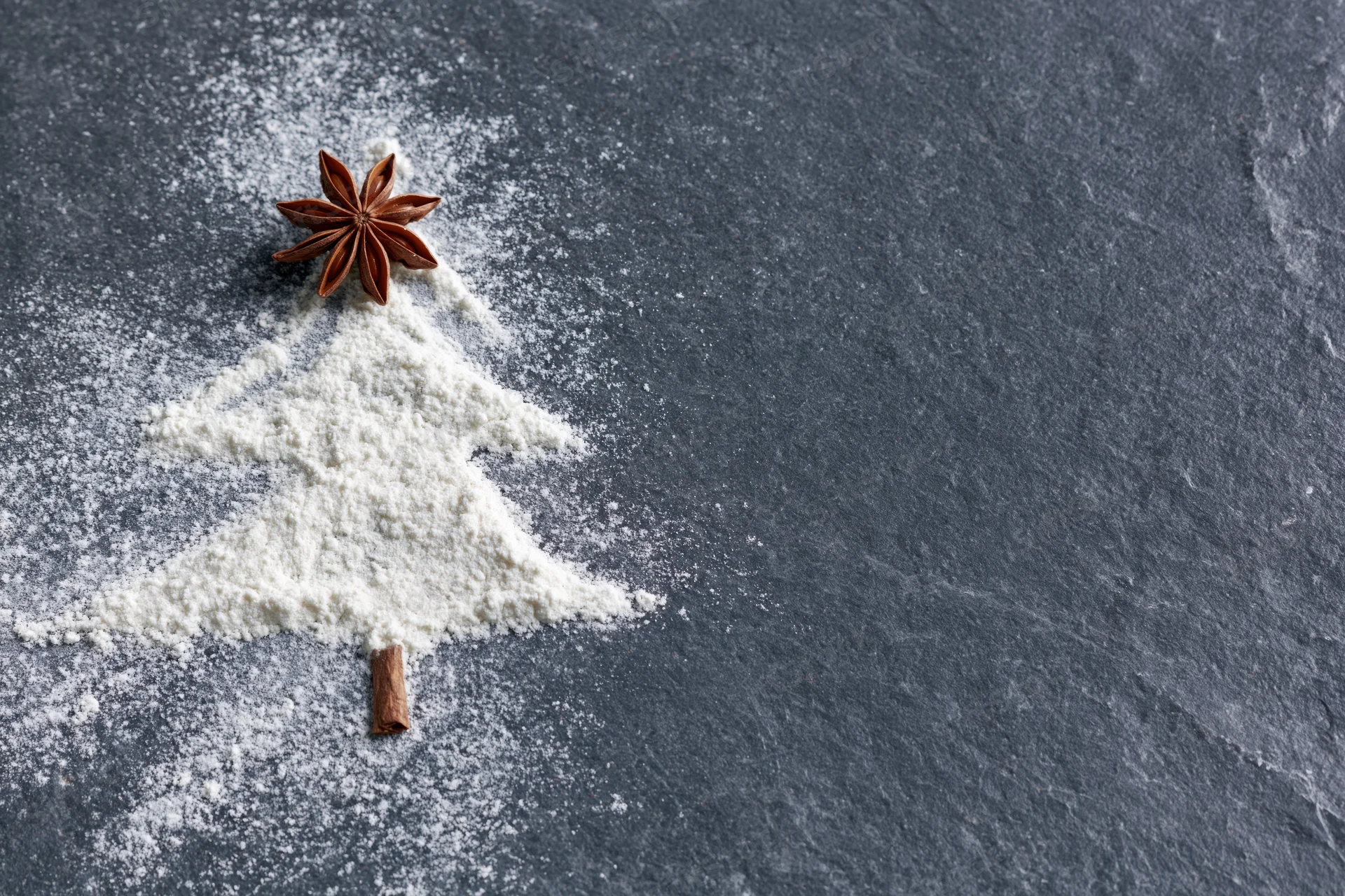 Flour shaped into a christmas tree with star anise and cinnamon stick on slate surface