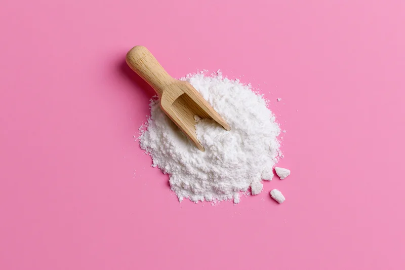 White powder with wooden scoop on pink background