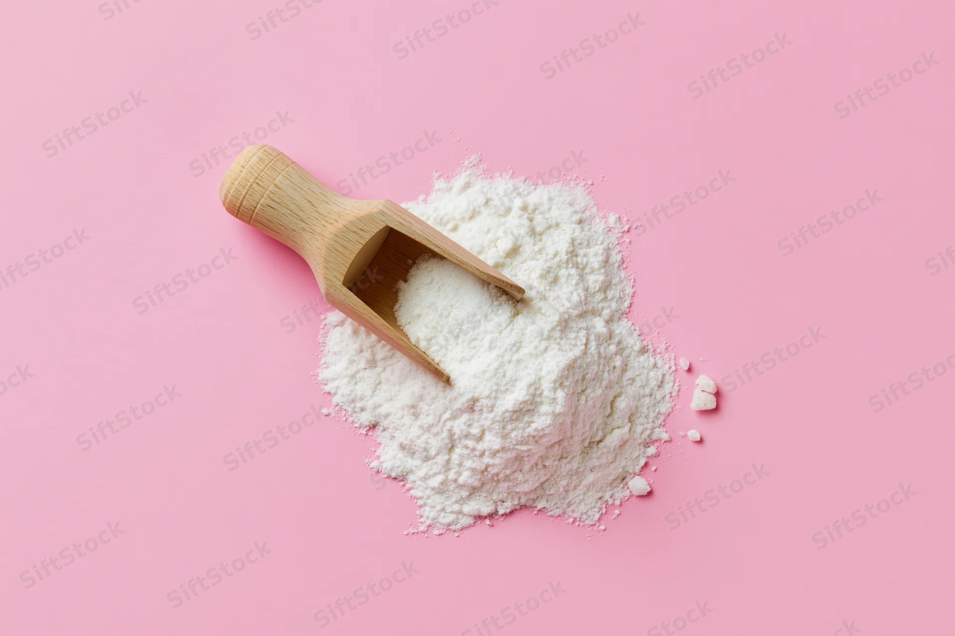 Wooden scoop resting in a pile of white flour on a pink background