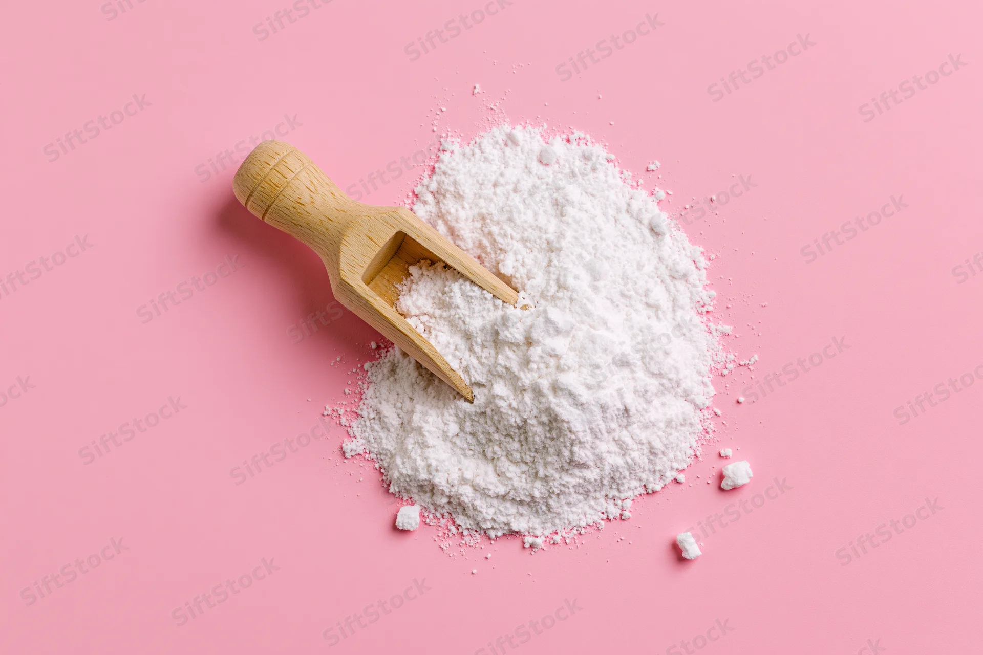 White powder with wooden scoop on pink background