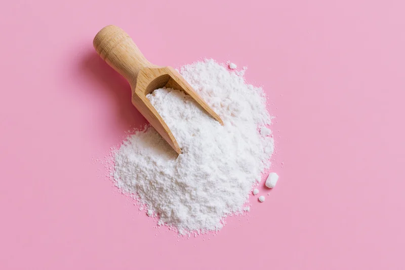 Wooden scoop resting in a pile of white powder on a pink surface