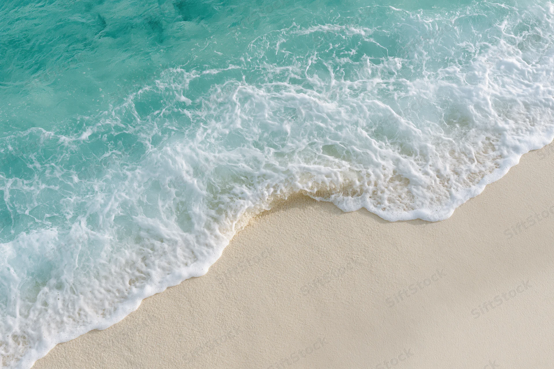 Turquoise ocean wave with white foam washing onto sandy beach