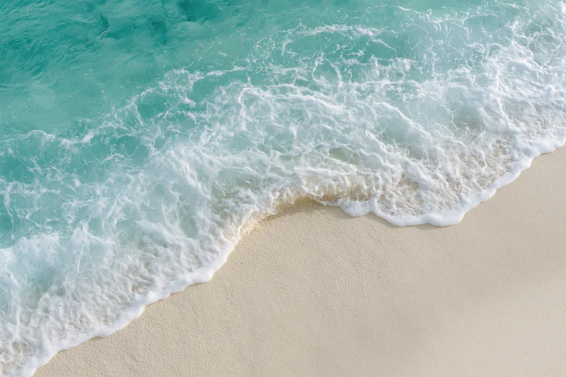 Turquoise ocean wave with white foam washing onto sandy beach