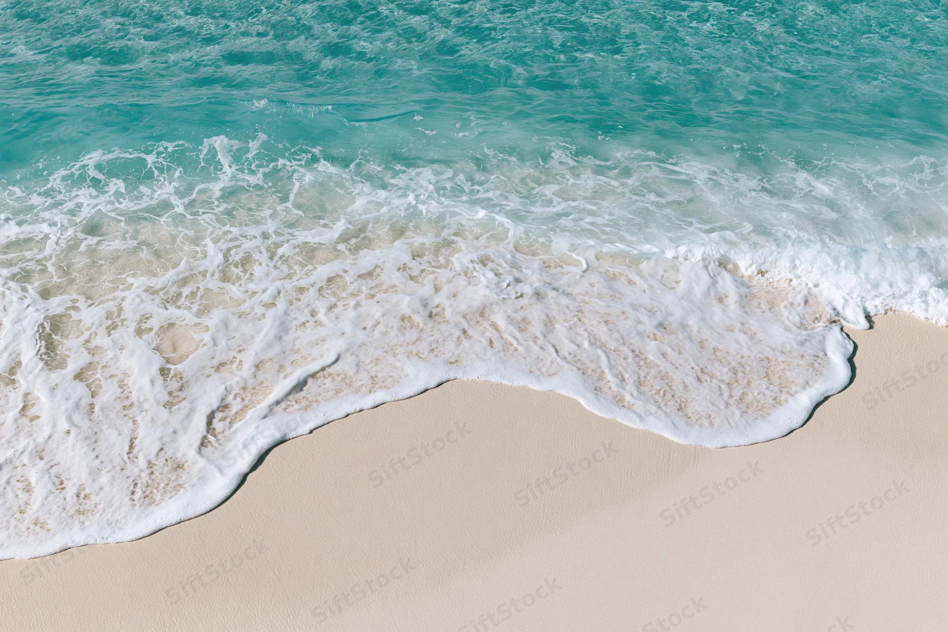 Waves breaking on a sandy beach with white foam and turquoise water