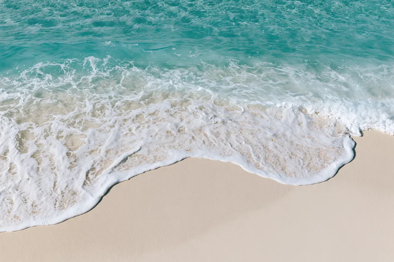 Waves breaking on a sandy beach with white foam and turquoise water