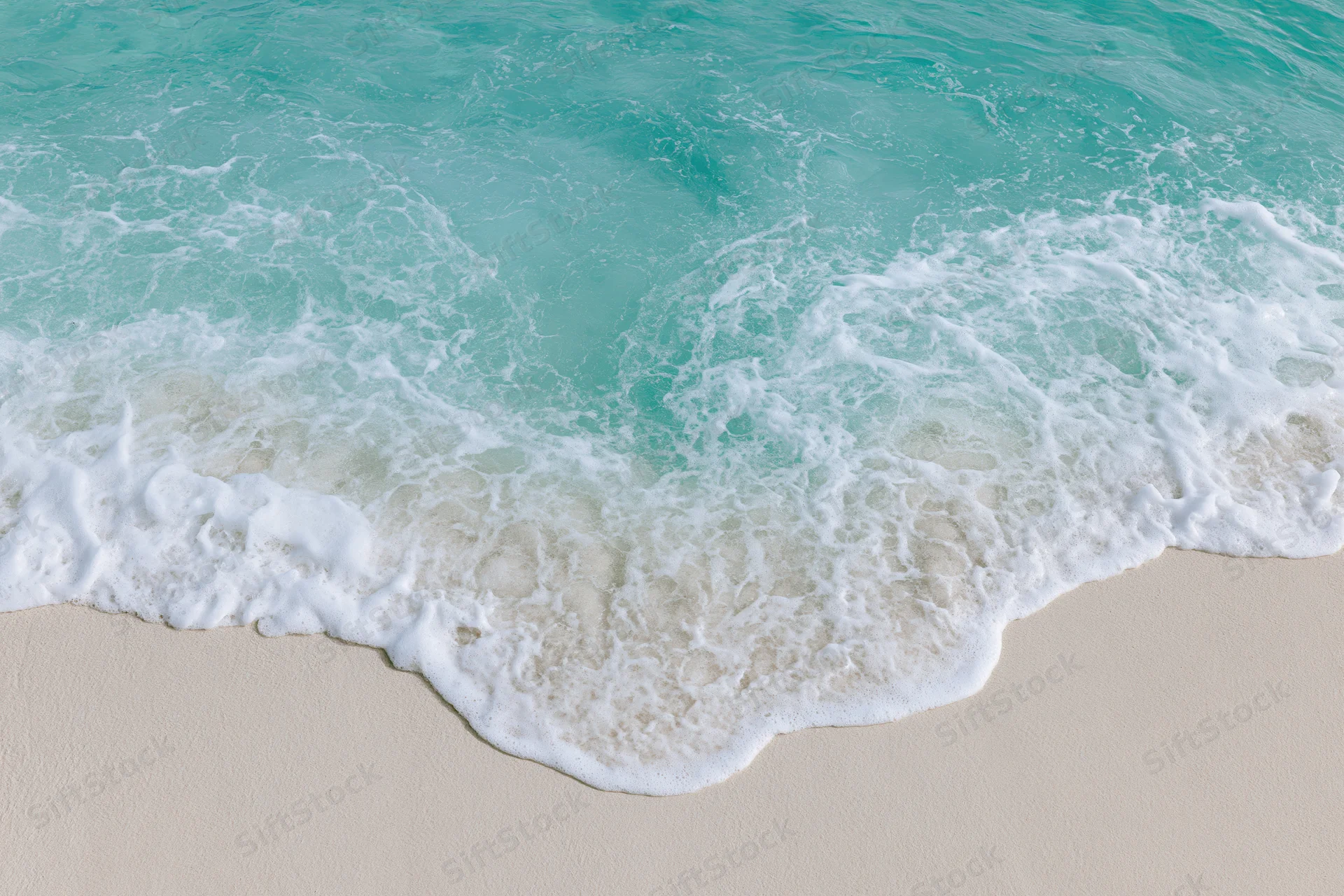 Turquoise ocean wave with white foam washing onto sandy beach