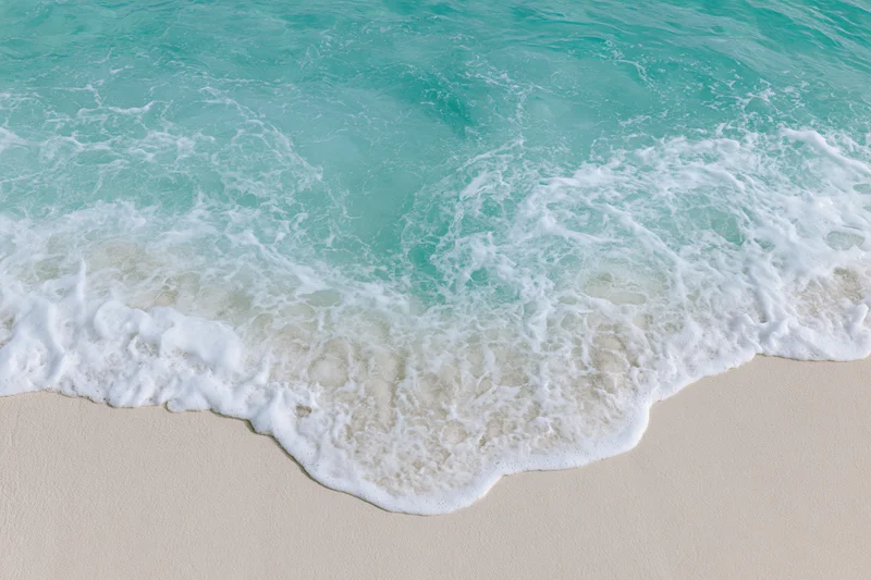 Turquoise ocean wave with white foam washing onto sandy beach