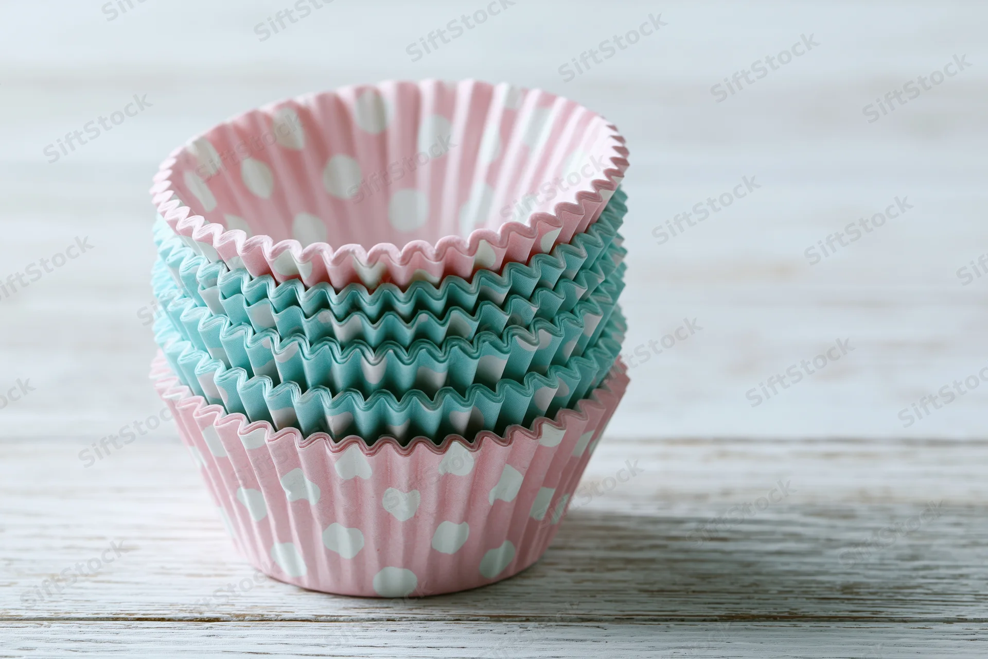 Stack of pink and blue polka dot cupcake liners on a white wooden table