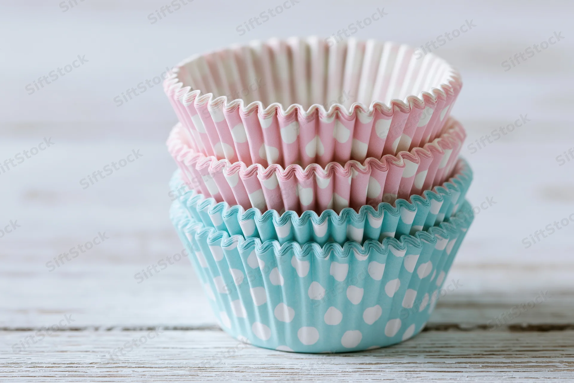 Stack of pink and blue polka dot cupcake liners on a light wooden surface