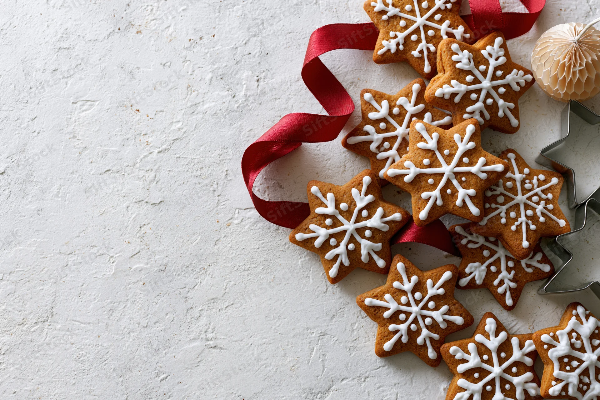 Snowflake-shaped gingerbread cookies with white icing and red ribbon arranged on textured white surface