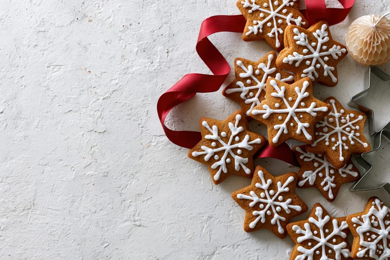 Snowflake-shaped gingerbread cookies with white icing and red ribbon arranged on textured white surface