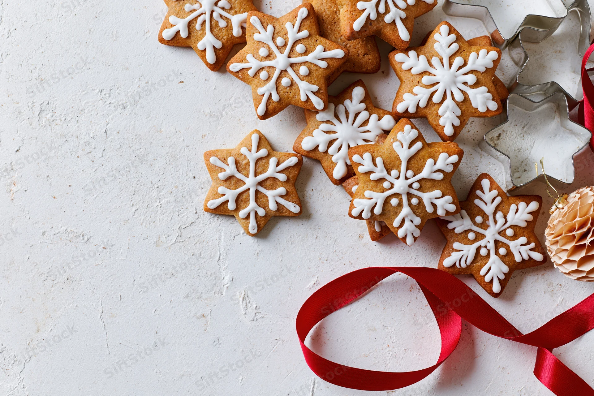Star-shaped gingerbread cookies with white icing and red ribbon on textured white surface