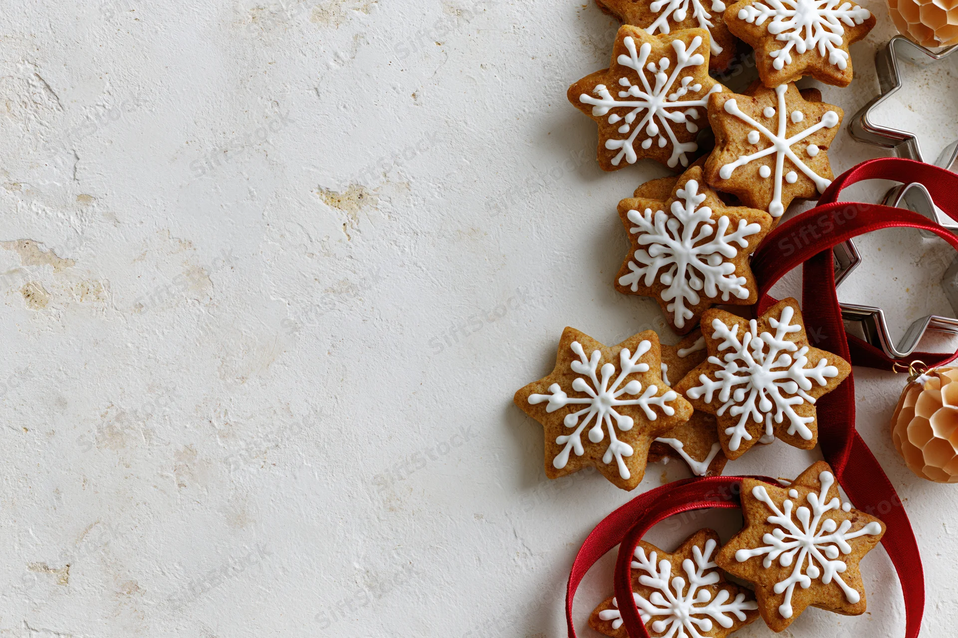 Gingerbread cookies shaped like snowflakes with white icing arranged on a textured white surface alongside red ribbon and metal cookie cutters