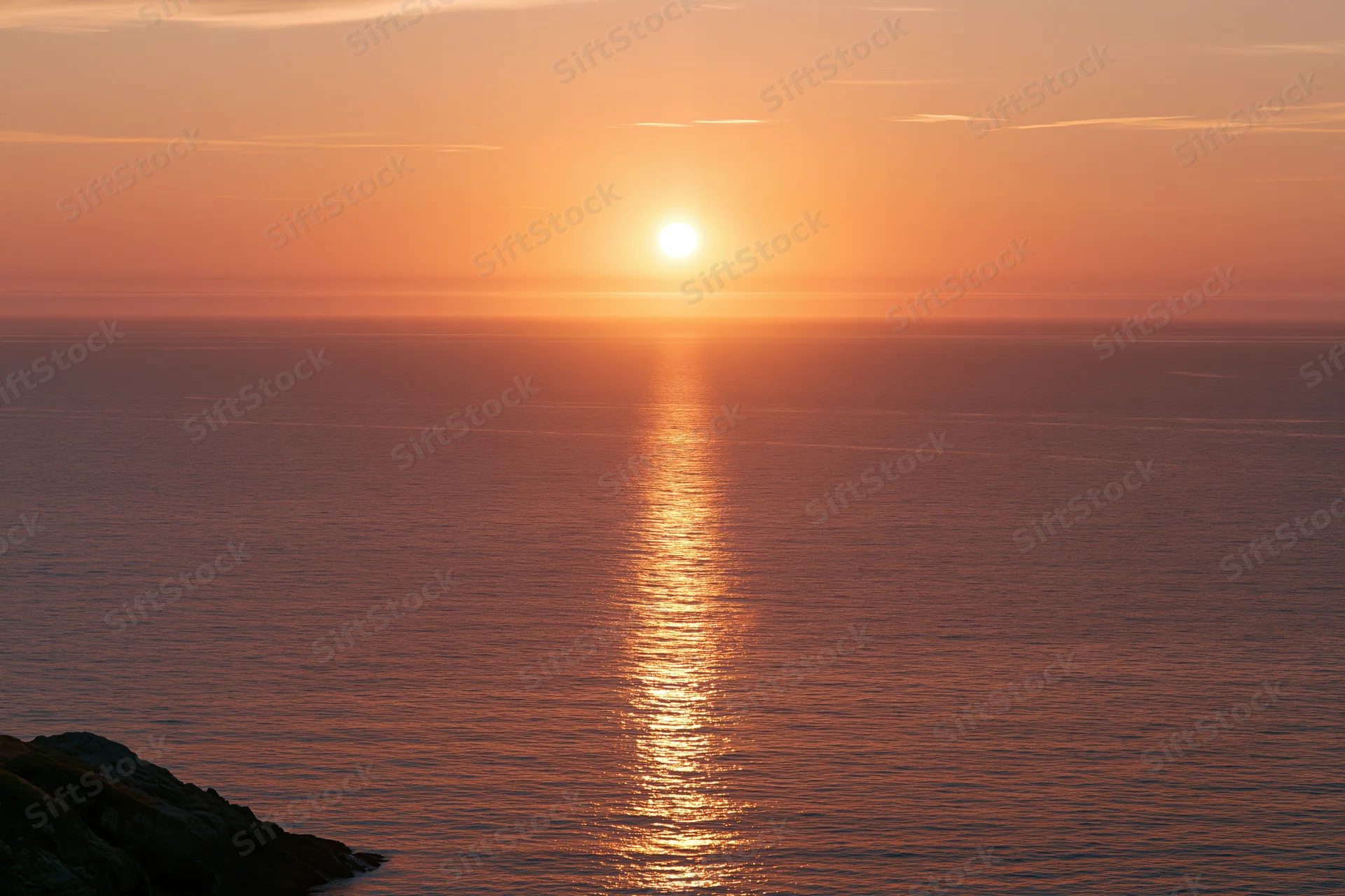 Sunset over calm ocean with sun reflection on water near rocky coastline