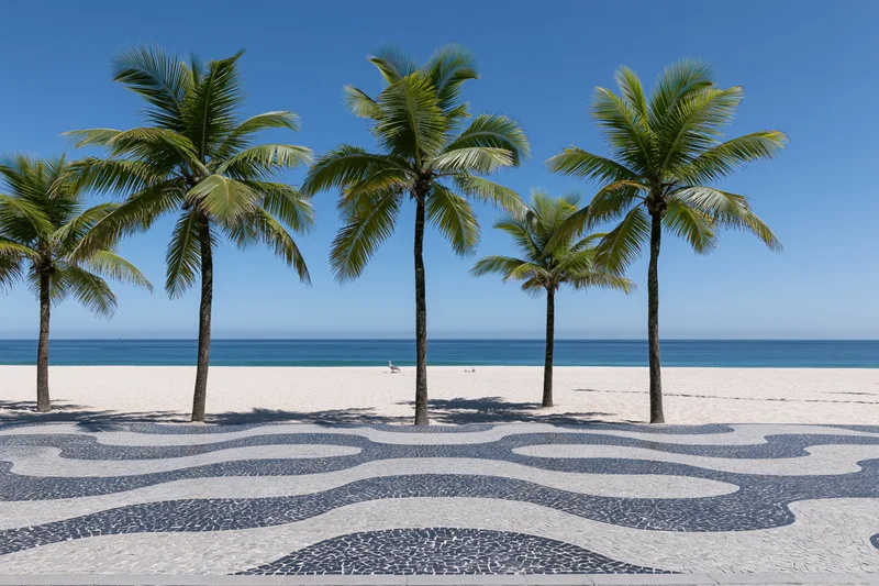 Palm trees lining a mosaic pavement beside a sandy beach with ocean and blue sky in the background