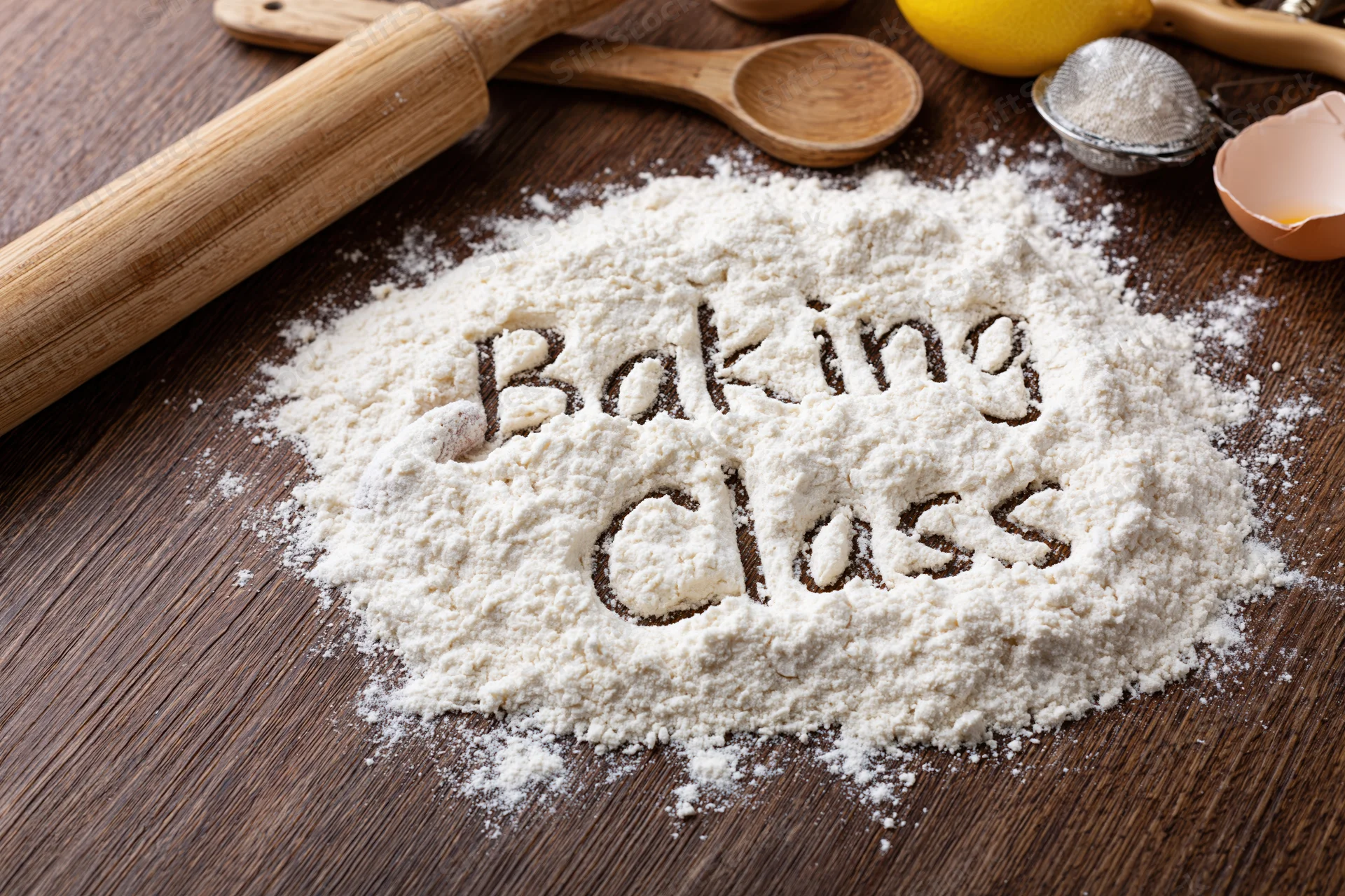 Flour with "baking class" written in it on a wooden countertop surrounded by baking tools