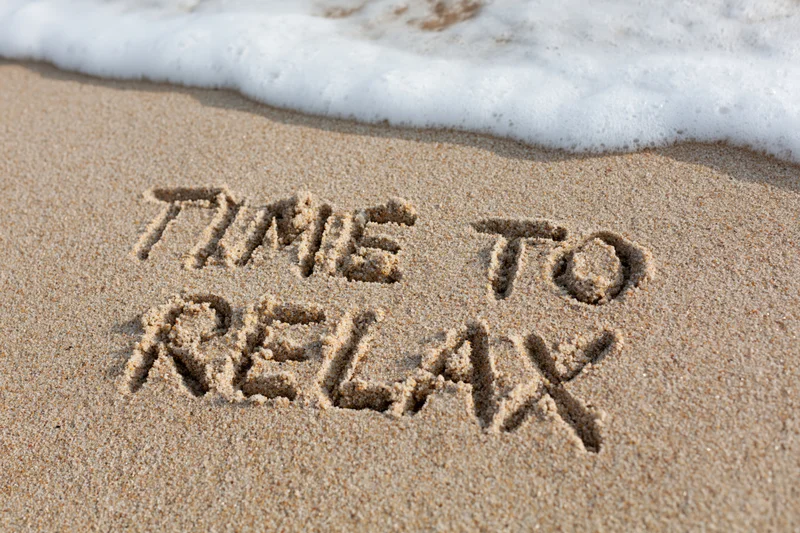 Words time to relax written in sand at beach with wave approaching