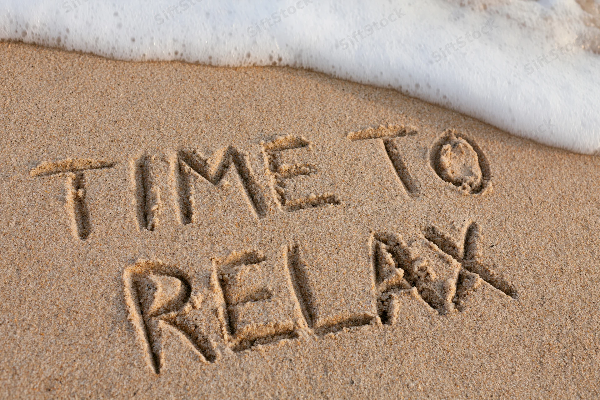 Time to relax written in sand at beach shoreline with wave approaching