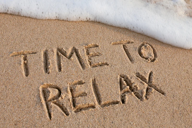 Time to relax written in sand at beach shoreline with wave approaching