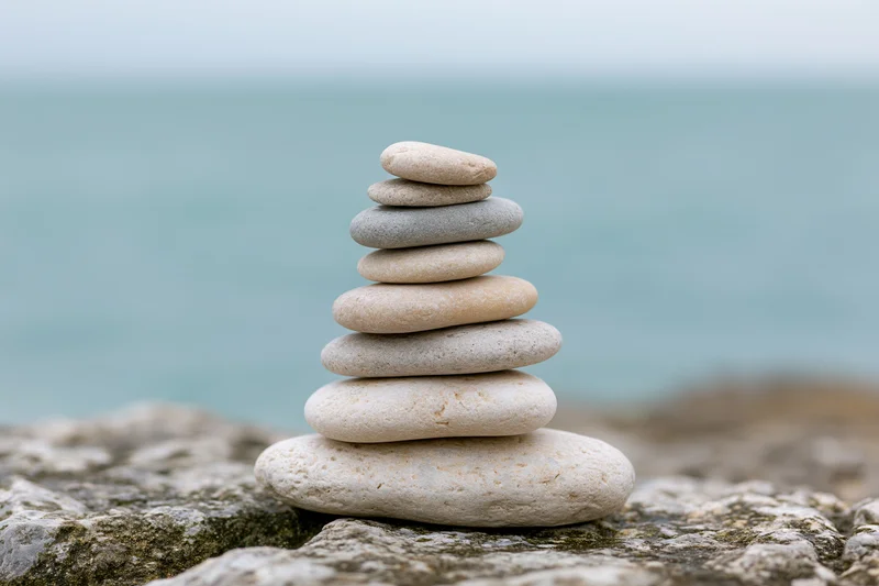 Stack of smooth stones balanced on rocky shore by ocean