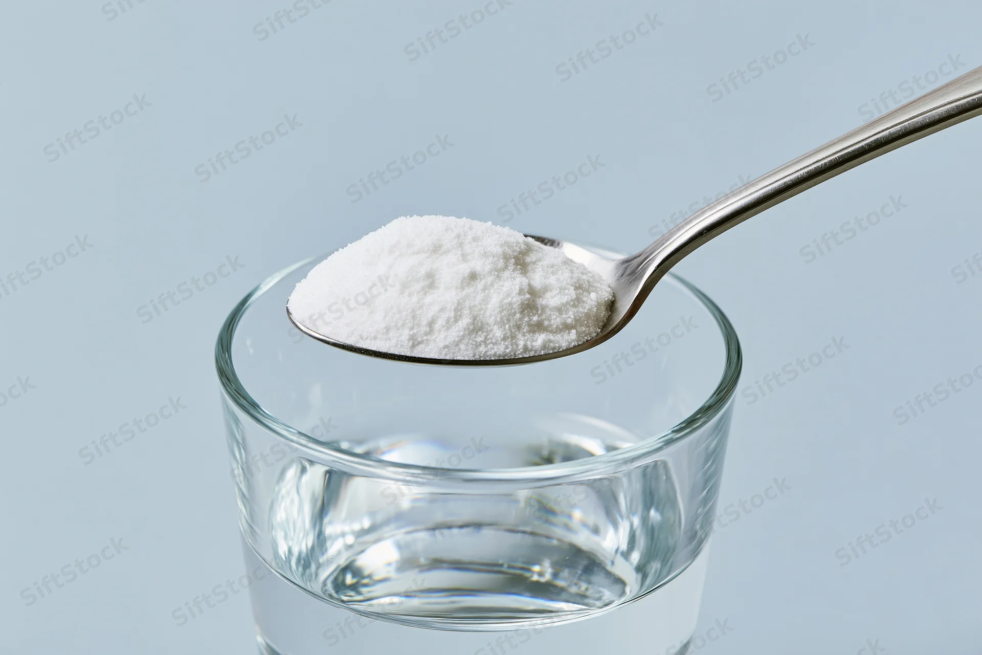 Spoon holding white powder above a glass of water