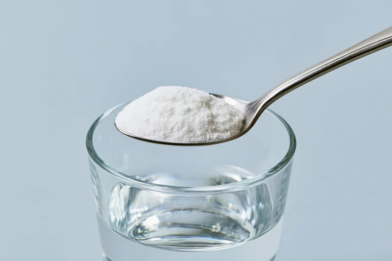 Spoon holding white powder above a glass of water