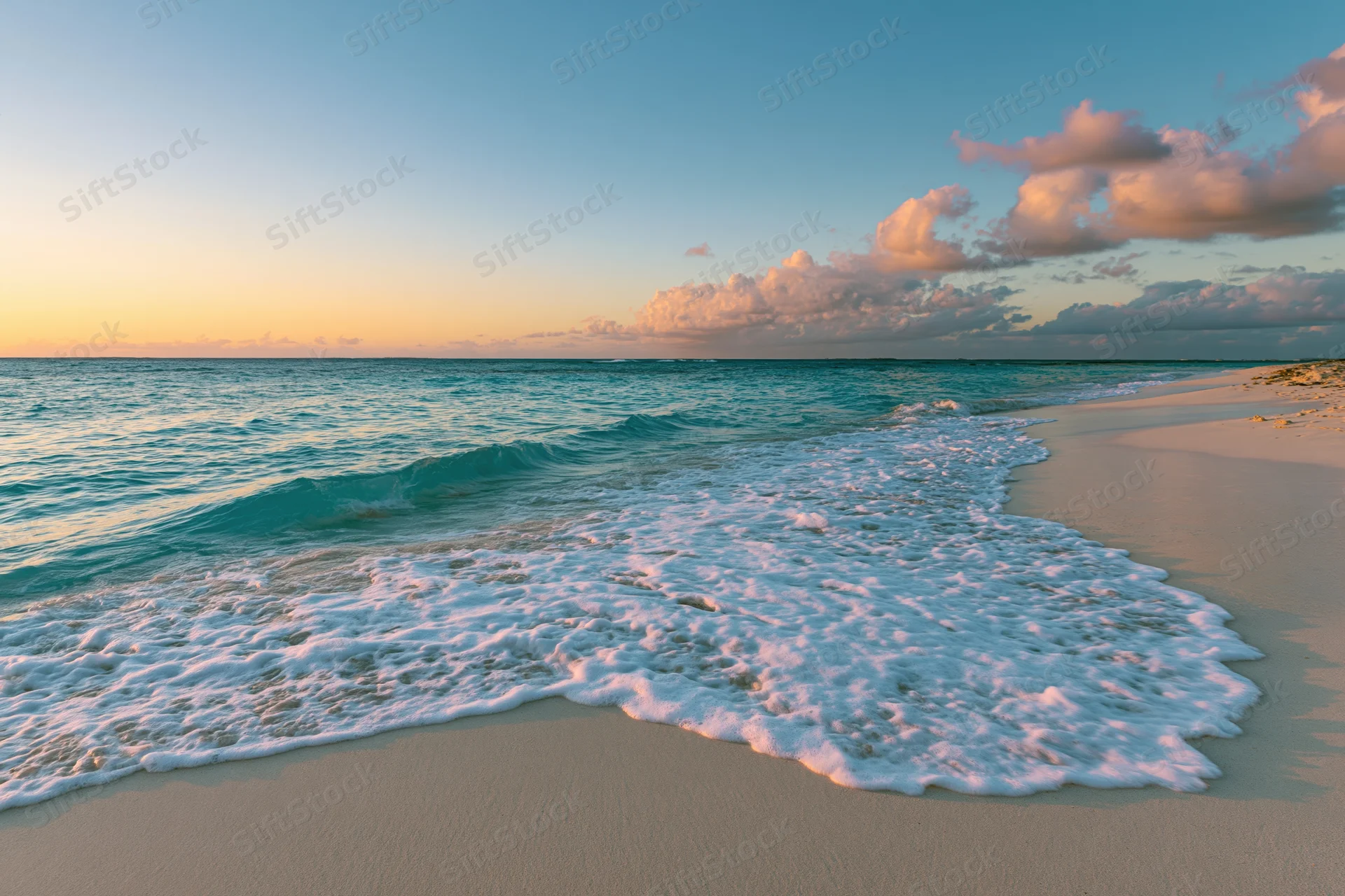 Gentle waves with white foam rolling onto sandy beach at sunset under pink and blue sky