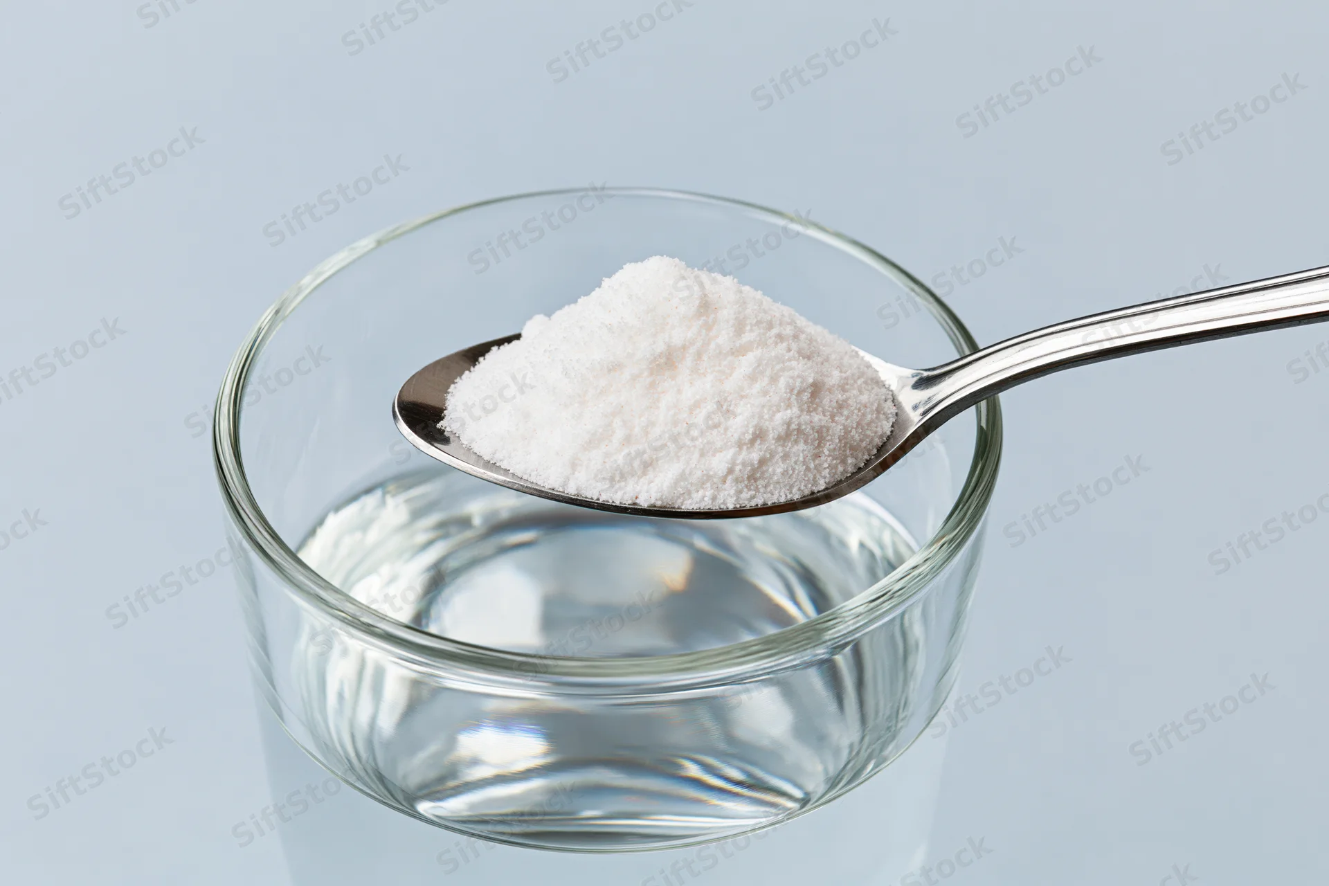 Spoon holding white powder above a glass of water