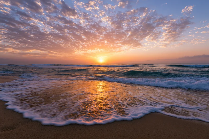 Sunset over ocean waves washing onto sandy beach at twilight