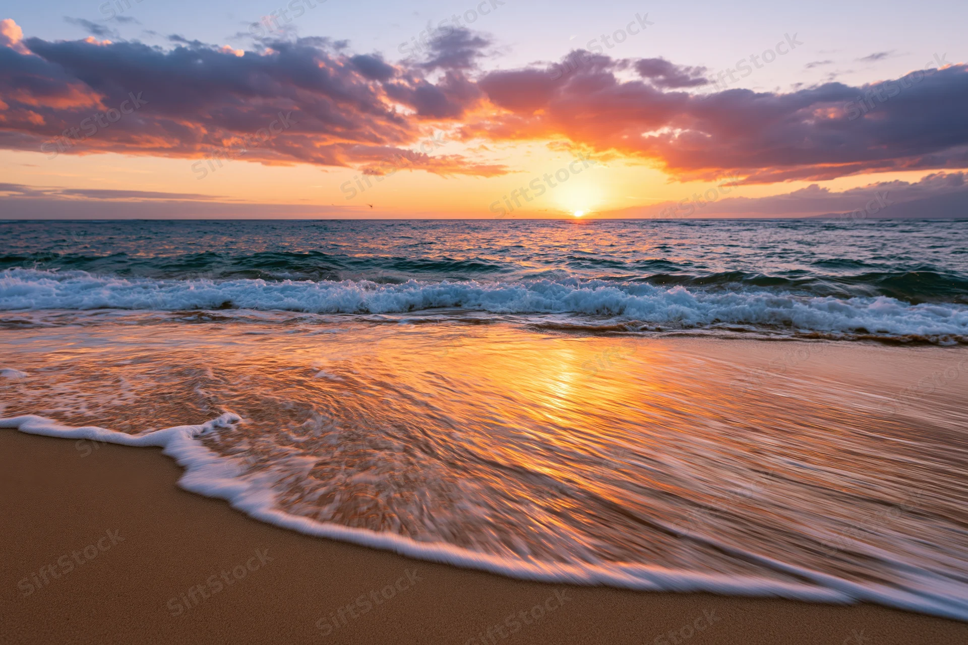 Sunset over ocean waves washing onto sandy beach at twilight
