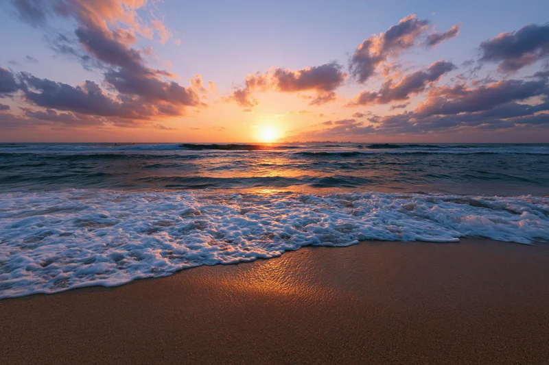 Sunset over ocean waves washing onto sandy beach at twilight
