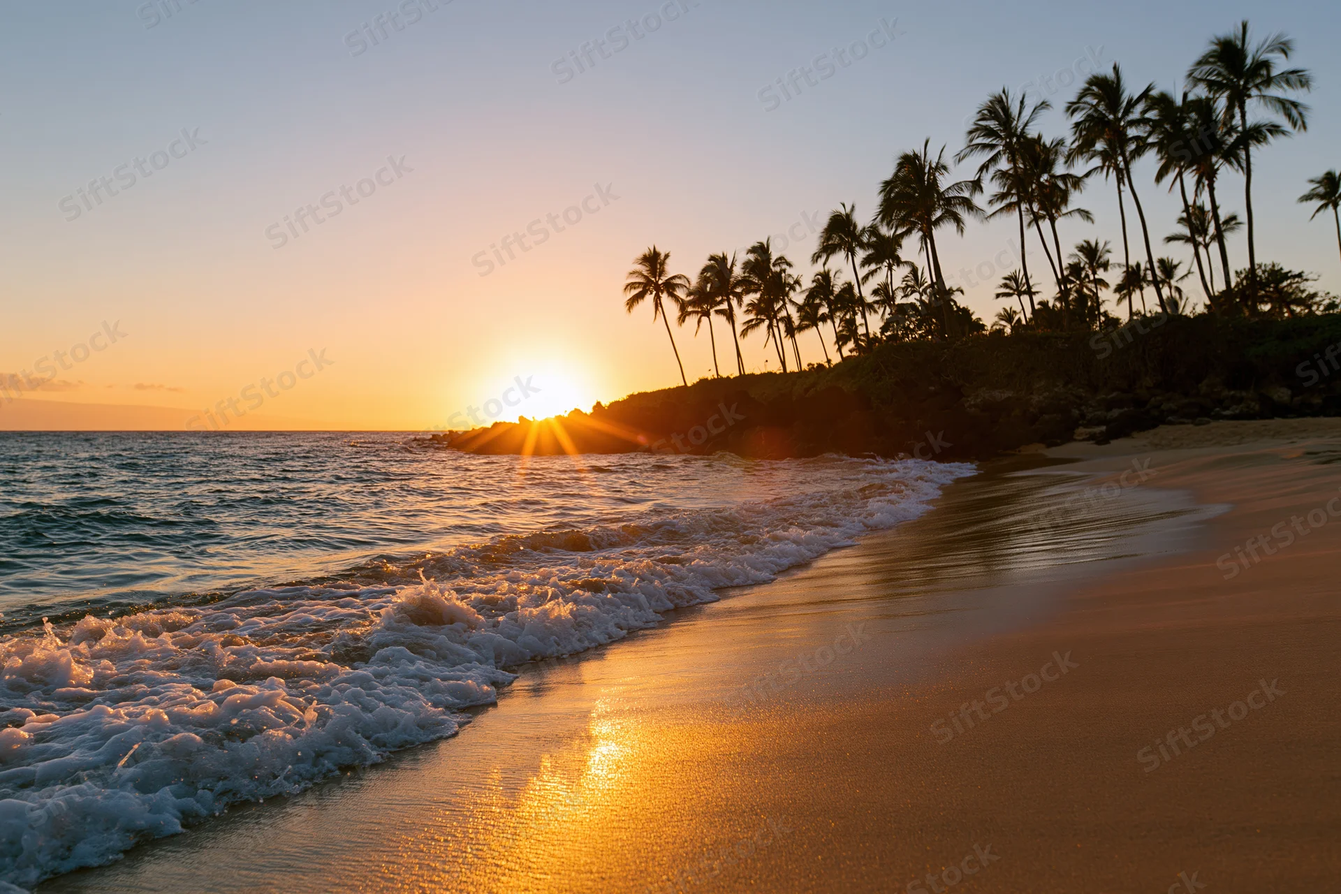 Sunset over tropical beach with palm trees and waves rolling onto sand