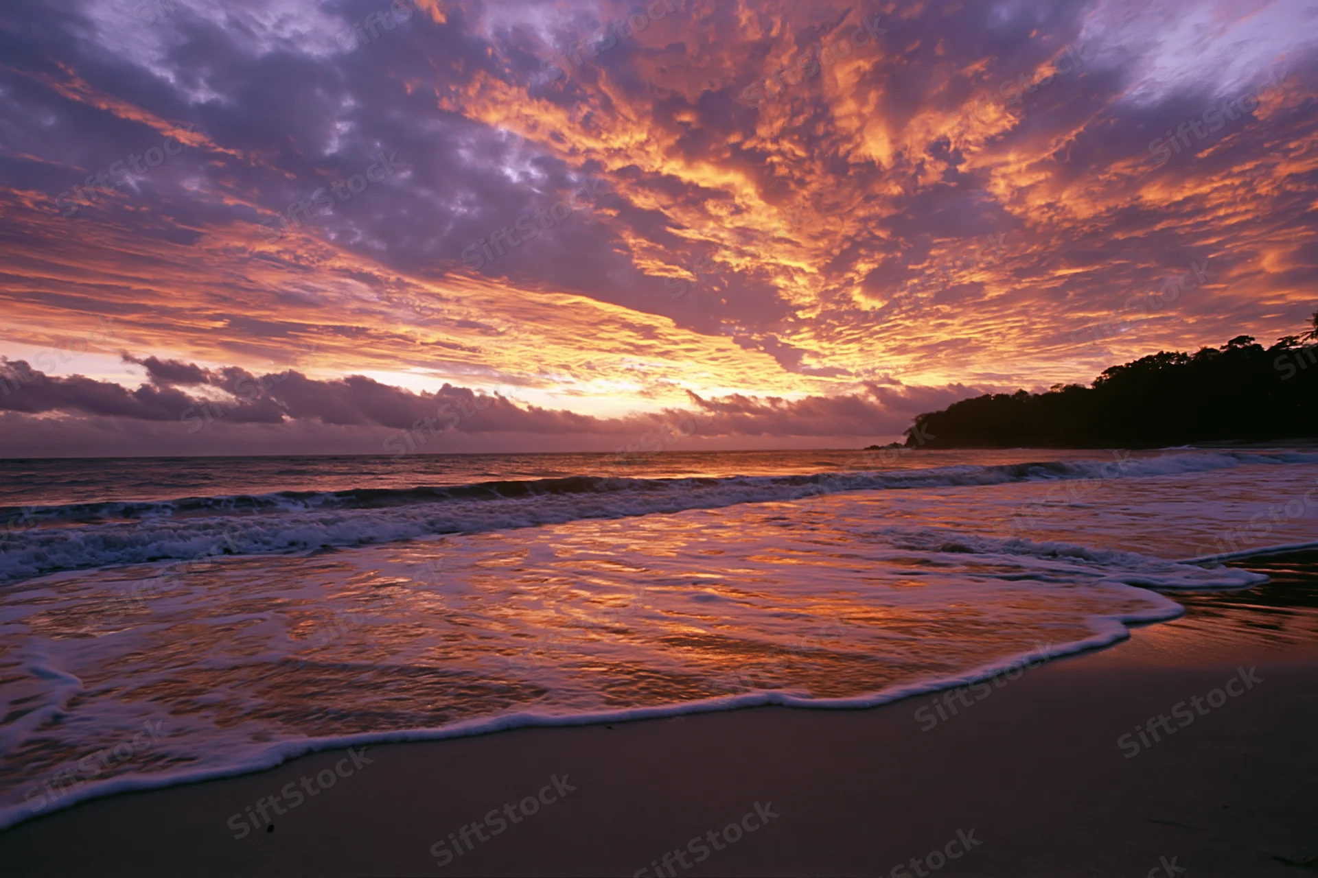 Sunset over ocean waves washing onto sandy beach with colorful clouds above