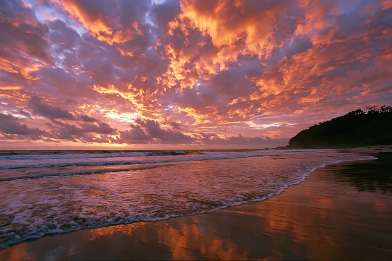 Vibrant sunset over a tropical beach with waves rolling onto the shore under a fiery sky