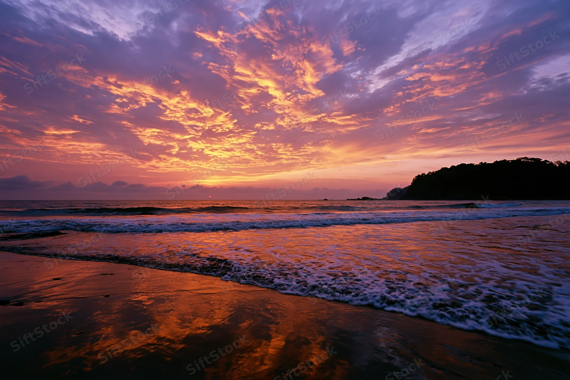 Vibrant sunset over ocean waves washing onto sandy beach at twilight