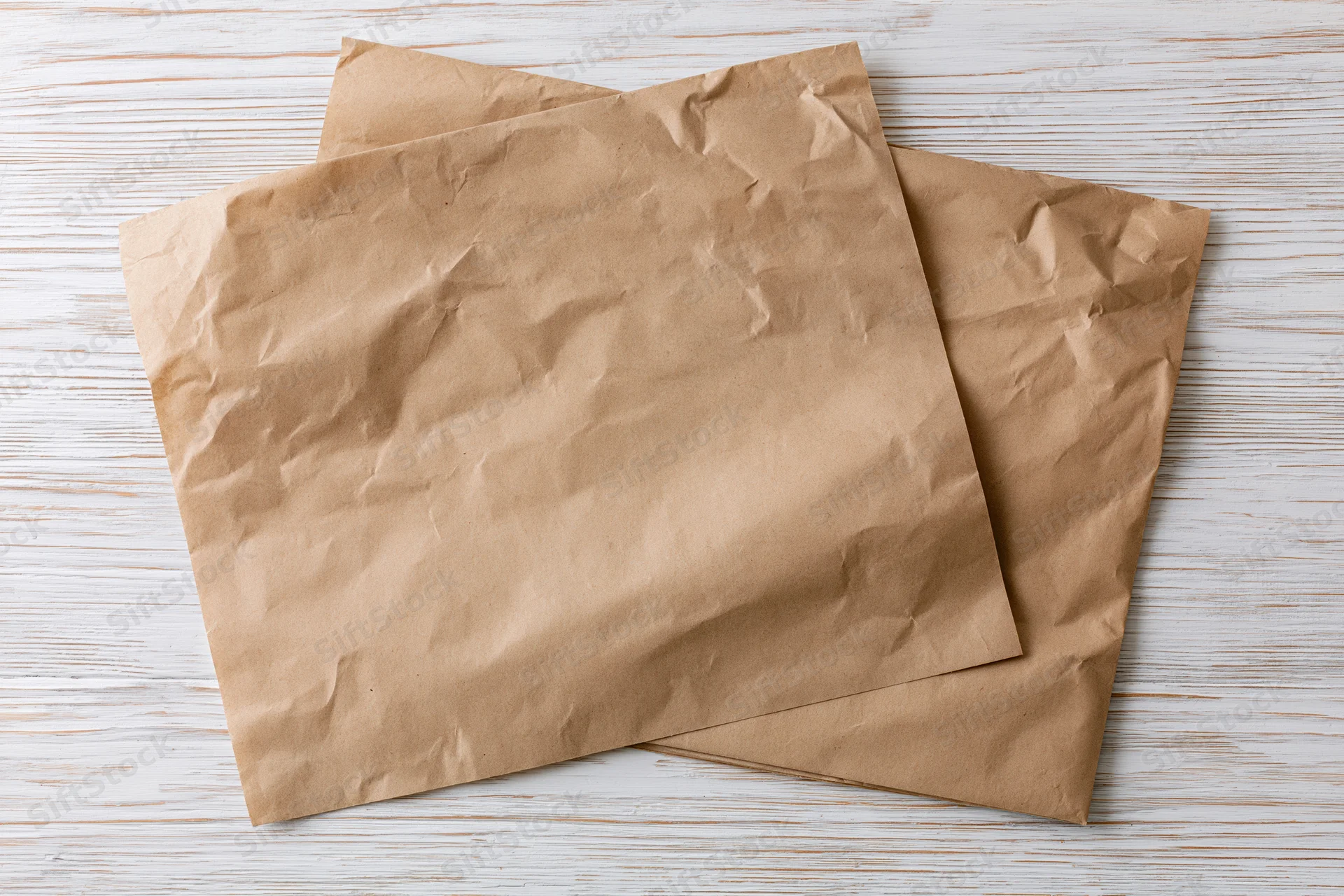 Two crumpled brown paper sheets on a white wooden surface