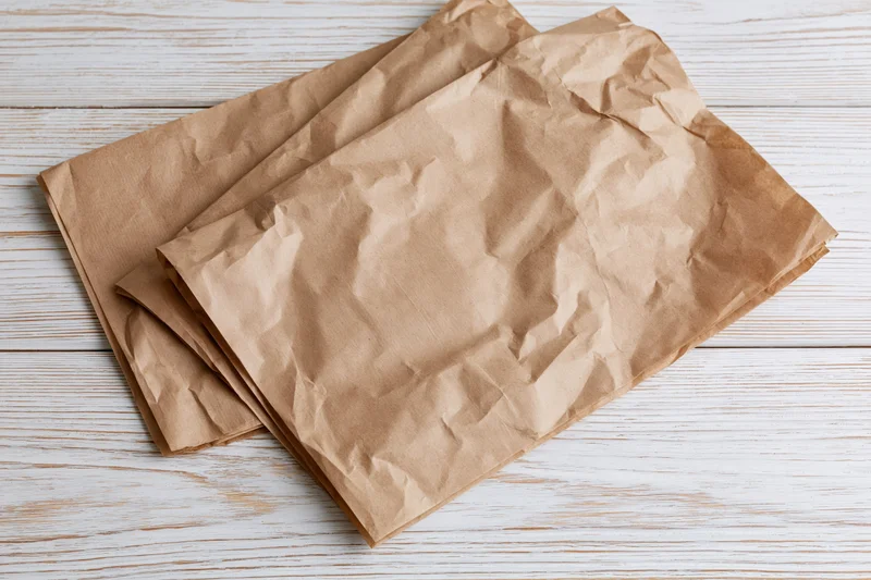 Crumpled brown paper sheets stacked on a white wooden surface